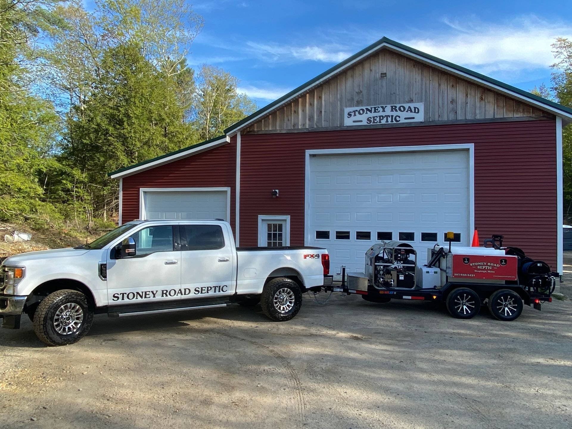 A white truck is parked in front of a red barn.