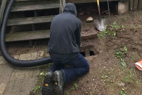 A man is kneeling down in the dirt next to a hose and a shovel.