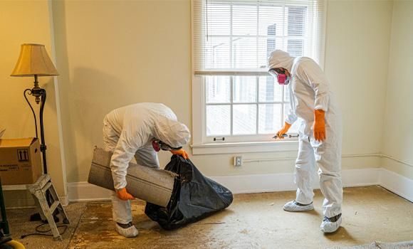 two men in protective suits are cleaning a room .