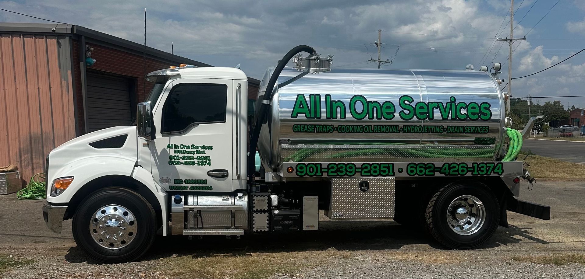 White and green truck parked beside a building and gravel lot