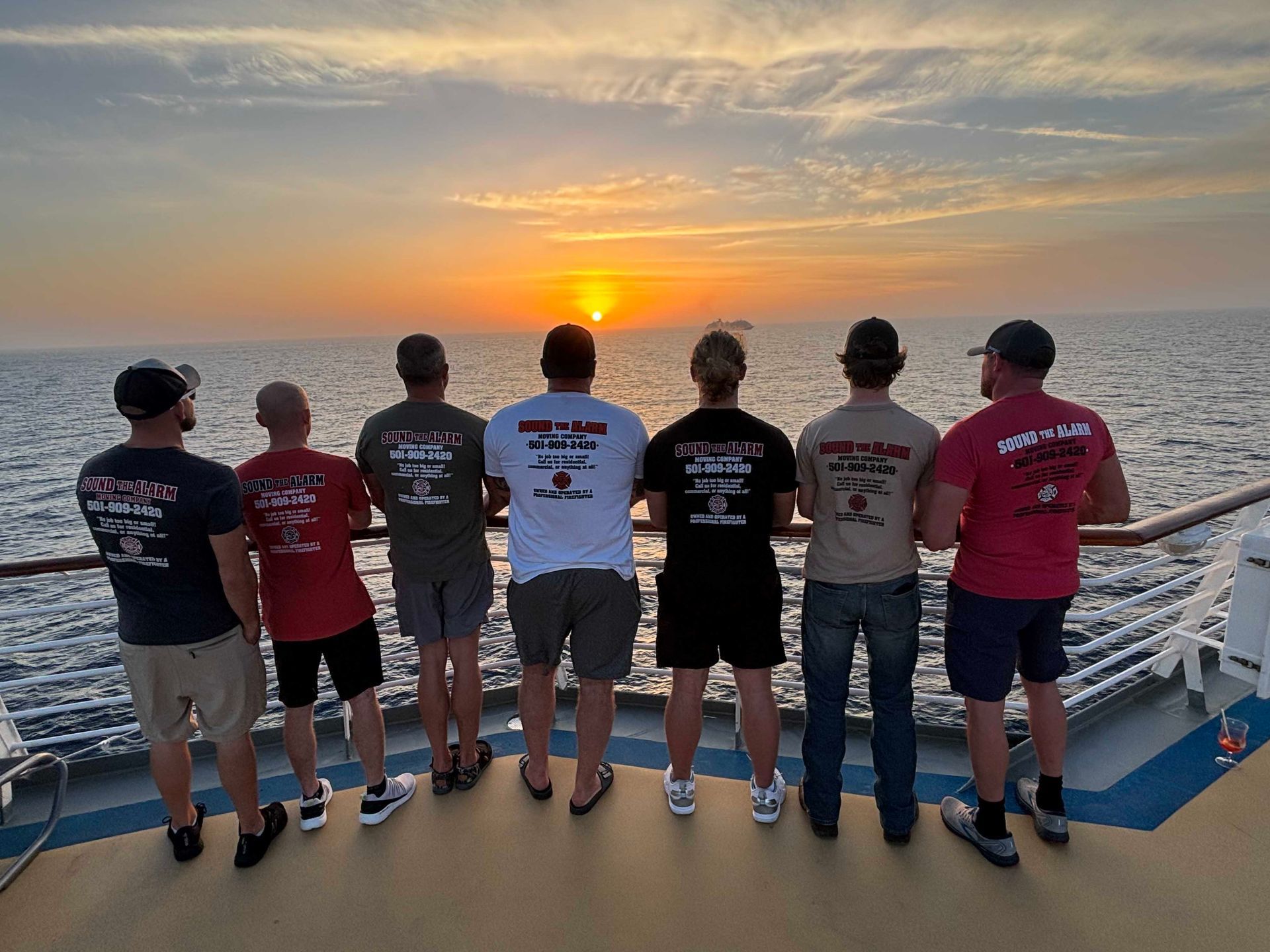Seven people watching a sunset over the ocean from a ship's deck.