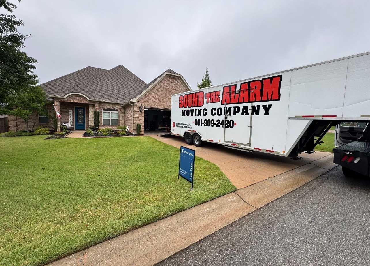 A moving truck is parked in front of a house. The truck is white with red lettering that says 