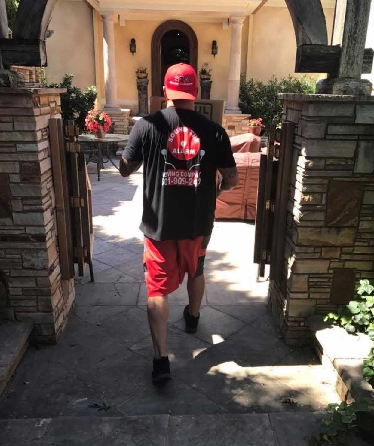 Person in red shorts and hat walks toward a building with stone pillars and a grand entrance.