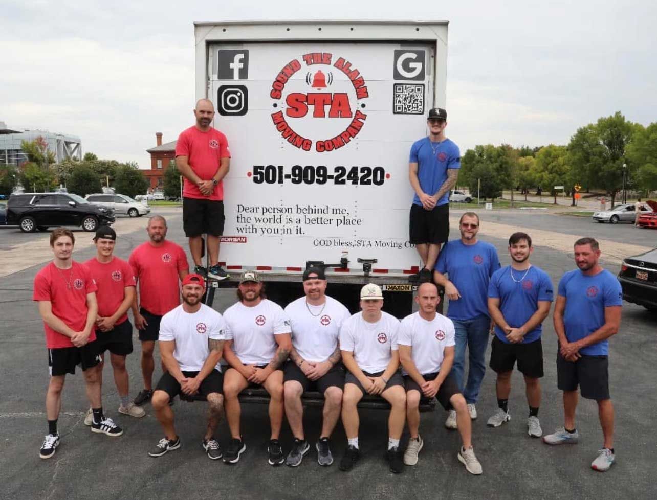 Moving crew poses in front of moving truck; red and blue shirts, logo on the truck.