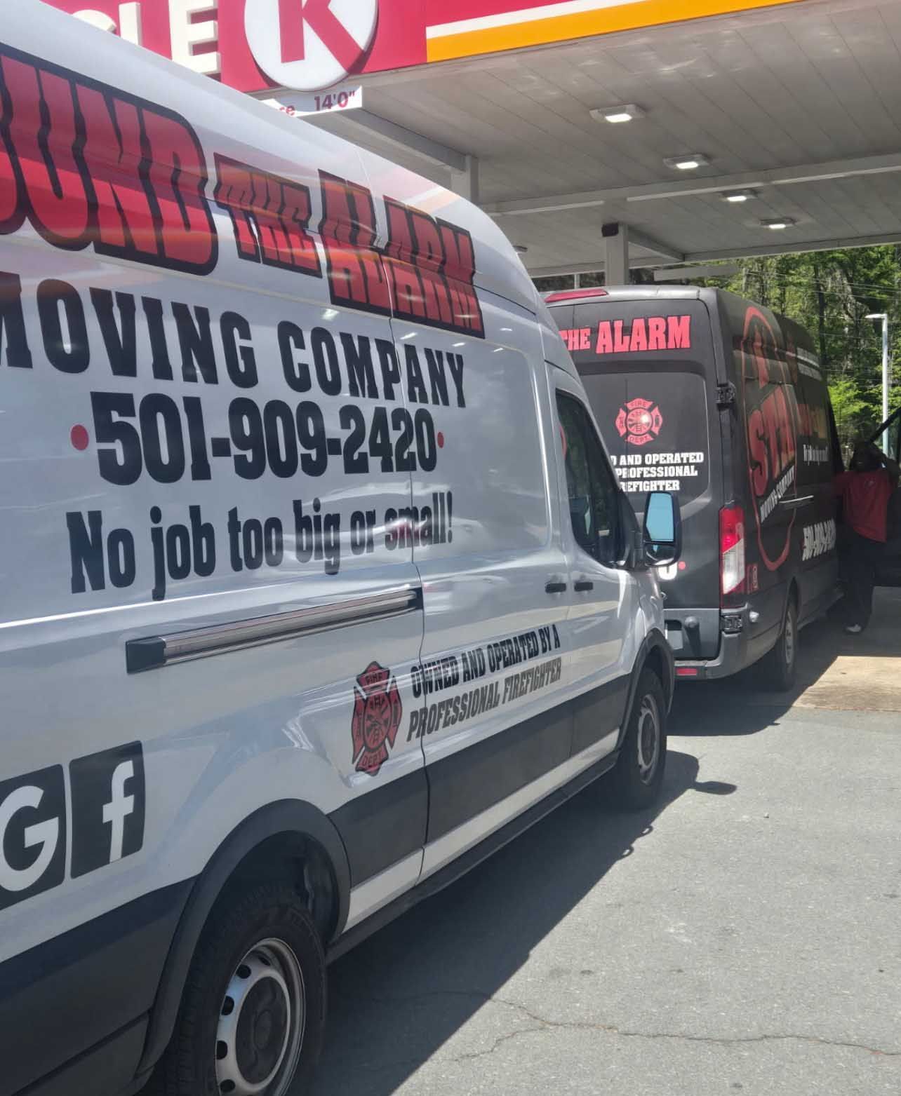 Two moving vans at a gas station, one white, one black, with company logo and phone number.