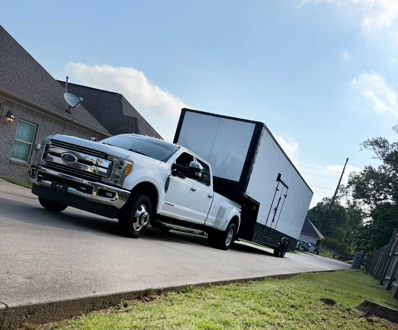 White truck towing a large enclosed trailer on a residential street under a blue sky.
