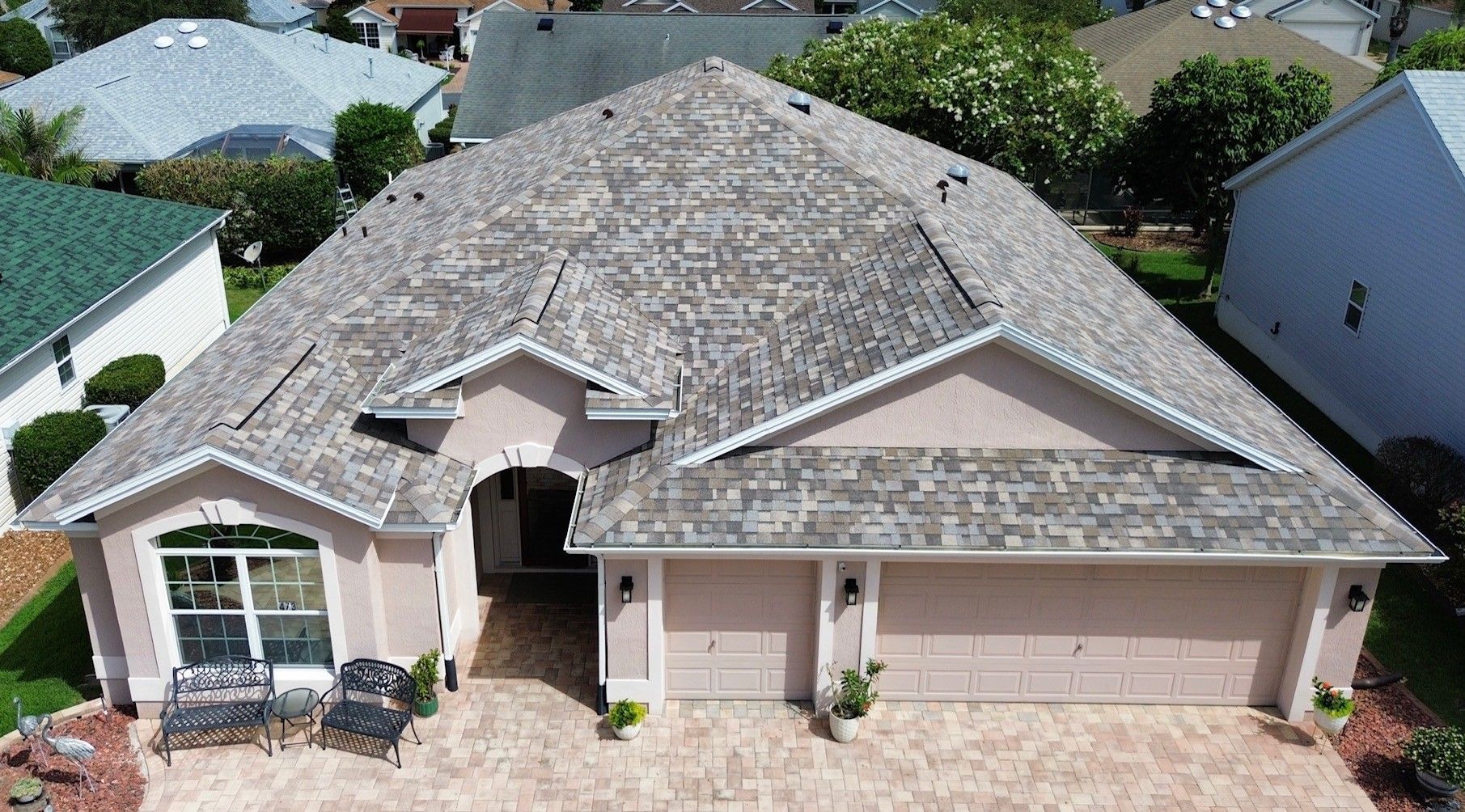 Suburban house with tan garage doors, stone driveway, and front porch under a partly cloudy sky