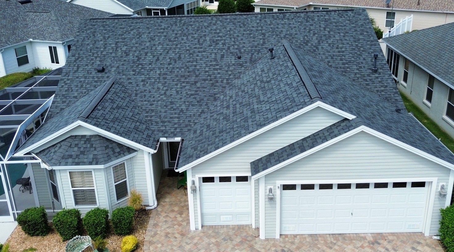Single-story white house with a gray roof, front lawn, flower beds, and a driveway.