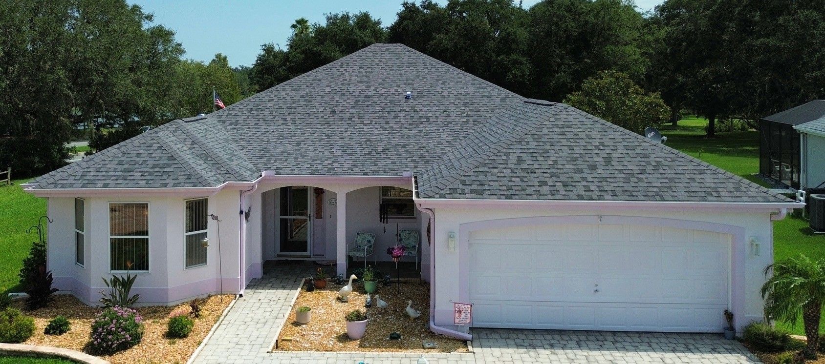Single-story beige house with a terracotta roof, manicured hedges, and a green lawn.