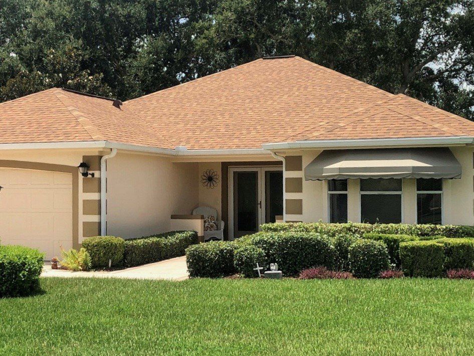 Single-story beige house with a terracotta roof, manicured hedges, and a green lawn.
