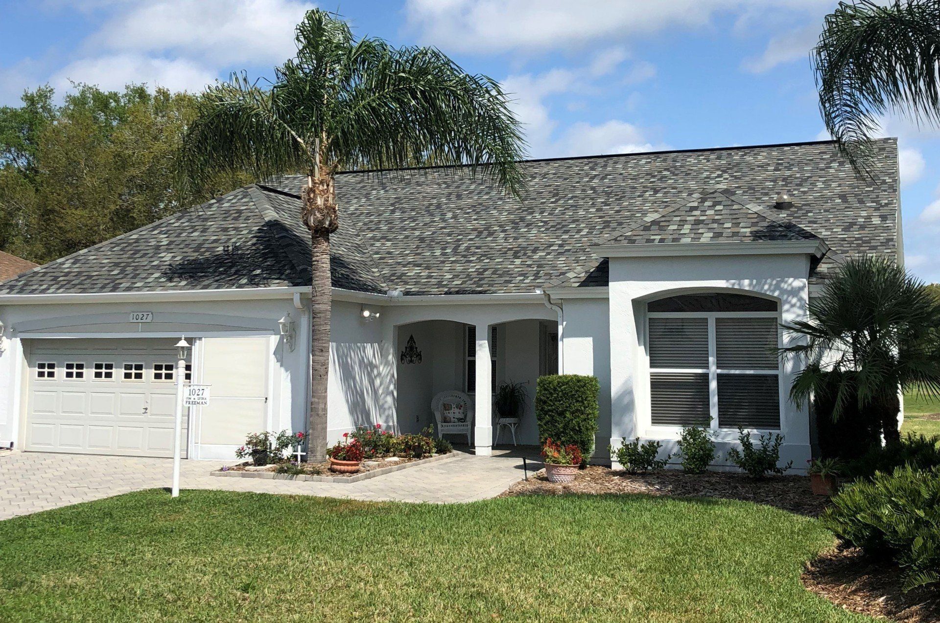 Suburban white house with gray roof, garage, front porch, and well-kept lawn under a blue sky