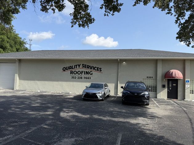 Quality Services Roofing office building with two parked cars and a red awning