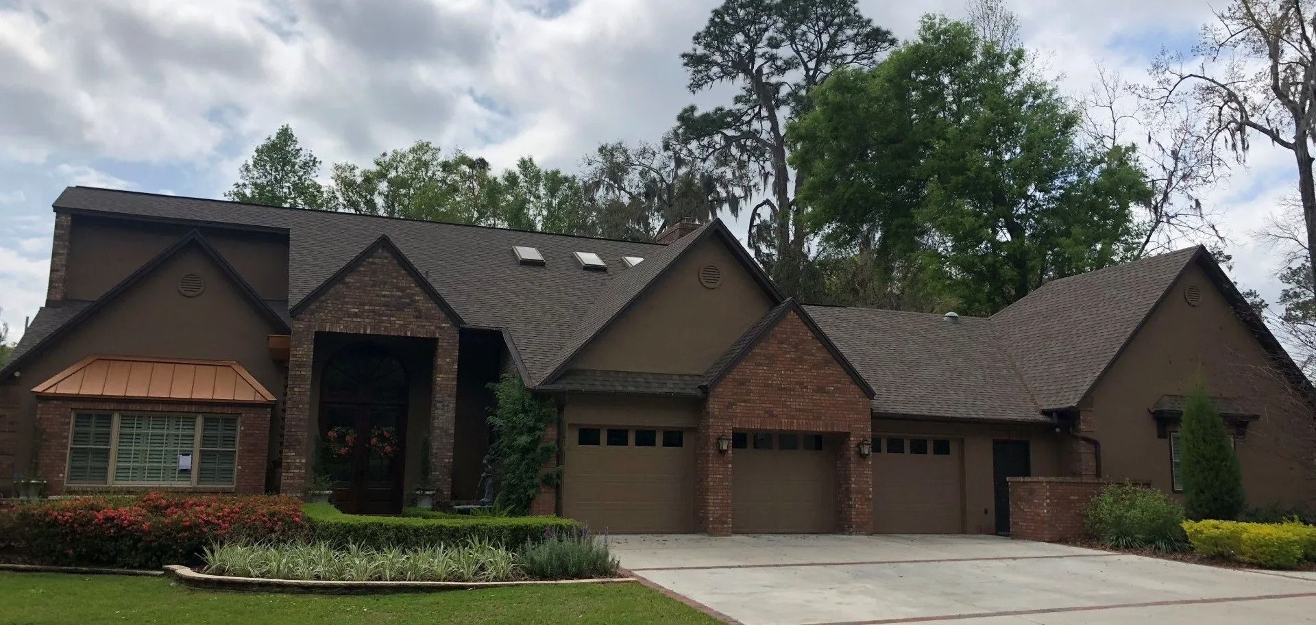 Brick suburban house with dark roof, arched windows, and a three-car garage under cloudy skies