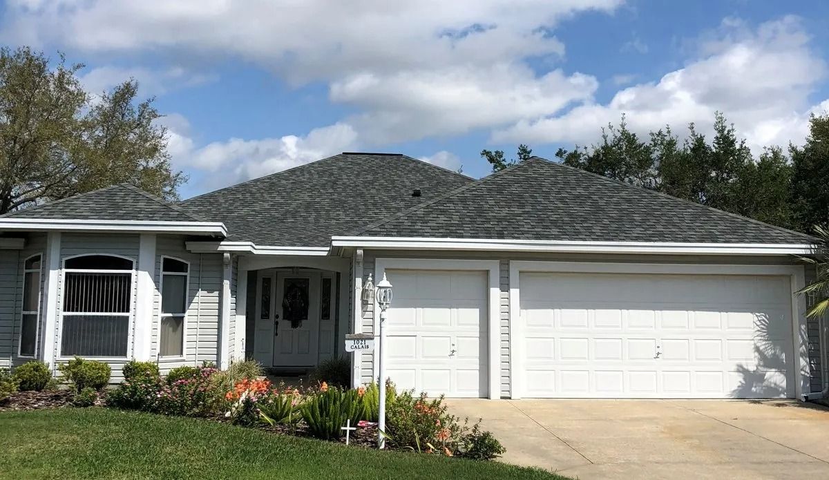 Single-story suburban house with a white garage, front porch, and manicured lawn under a cloudy sky