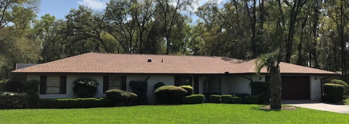 Single-story house with a red roof, white walls, and manicured lawn surrounded by trees