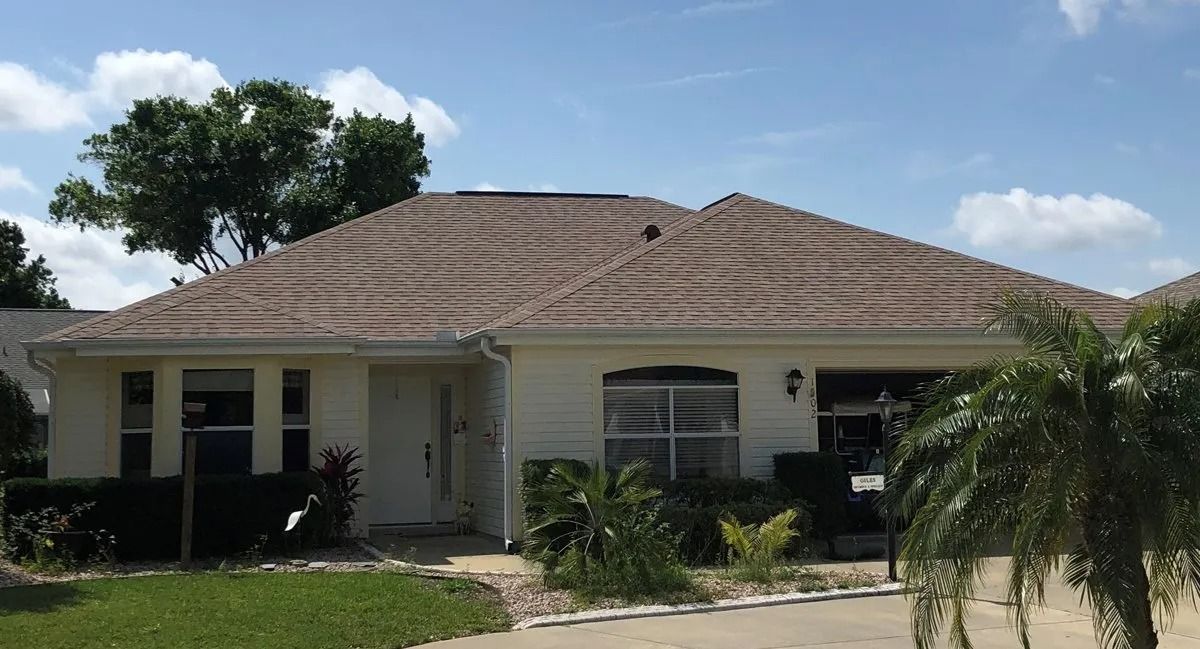 Single-story house with a tan tiled roof, white exterior, front porch, and palm trees in the yard
