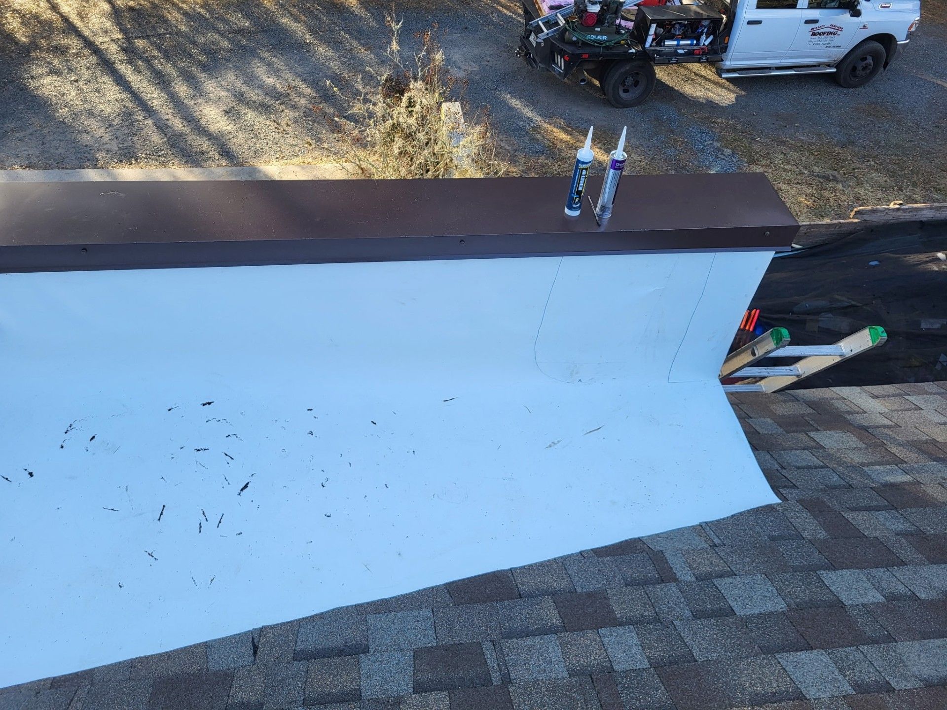 White roof repair area with dark brown trim, tools on top, and a gravel yard with vehicles in the background