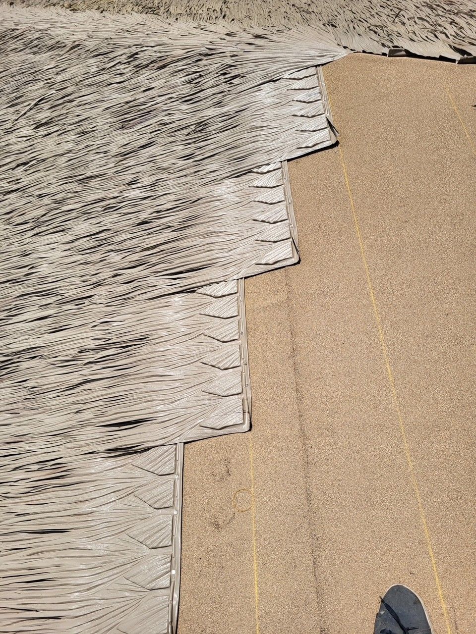 Worn rug edge beside beige carpet with visible frayed layers and stitching