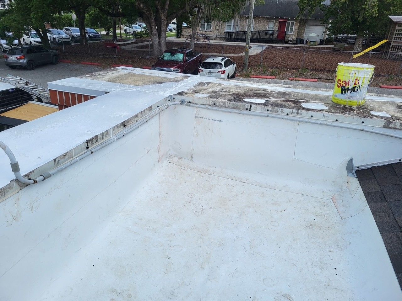 White rooftop with a built-up parapet and drains, overlooking parked cars and trees below.