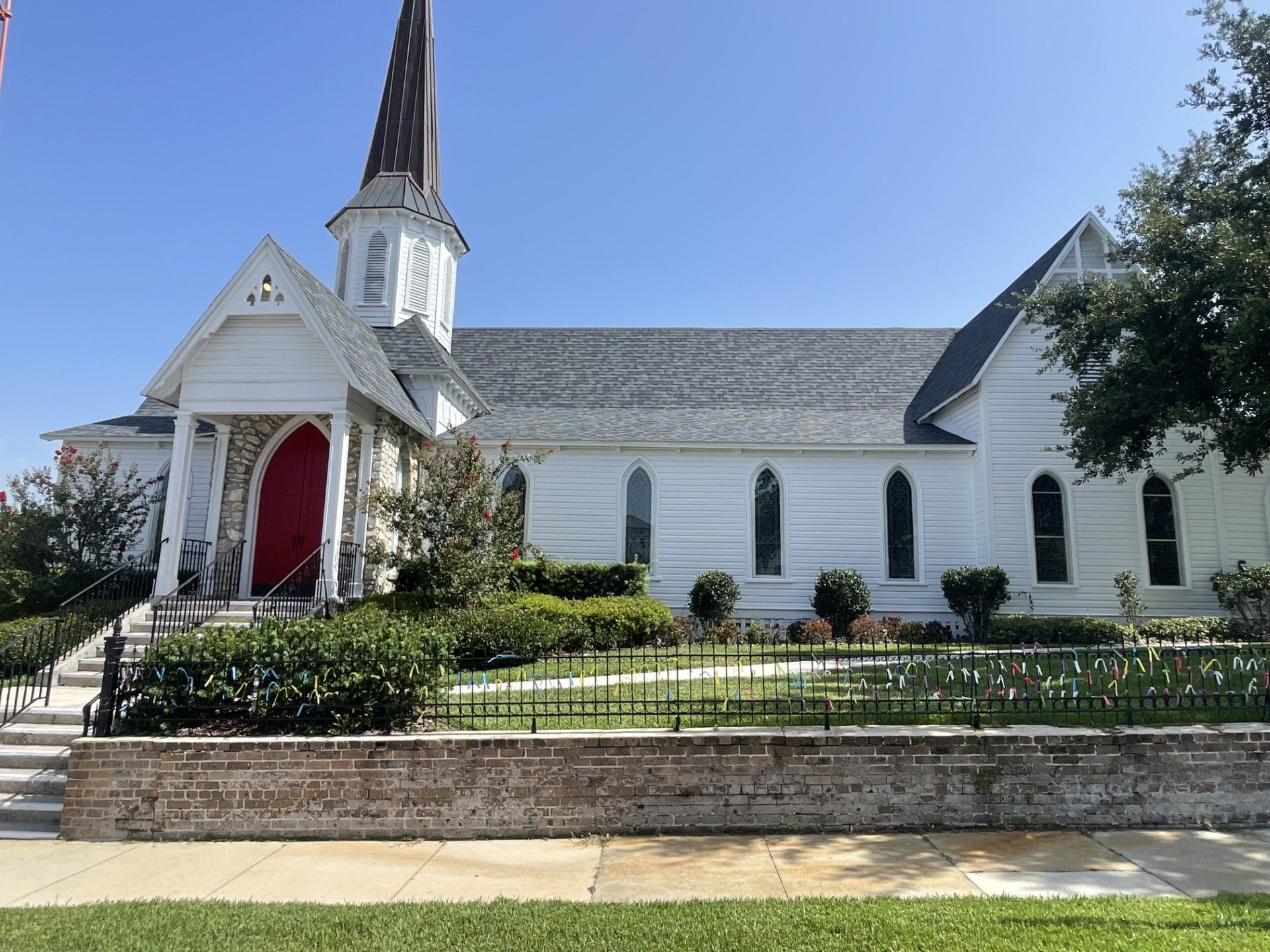 White church with a tall steeple, red door, and manicured front lawn under a clear blue sky