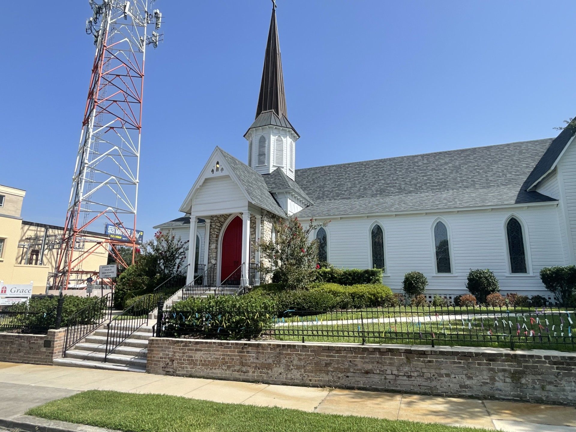 White church with a tall steeple and red arched door beside a communications tower under a blue sky.