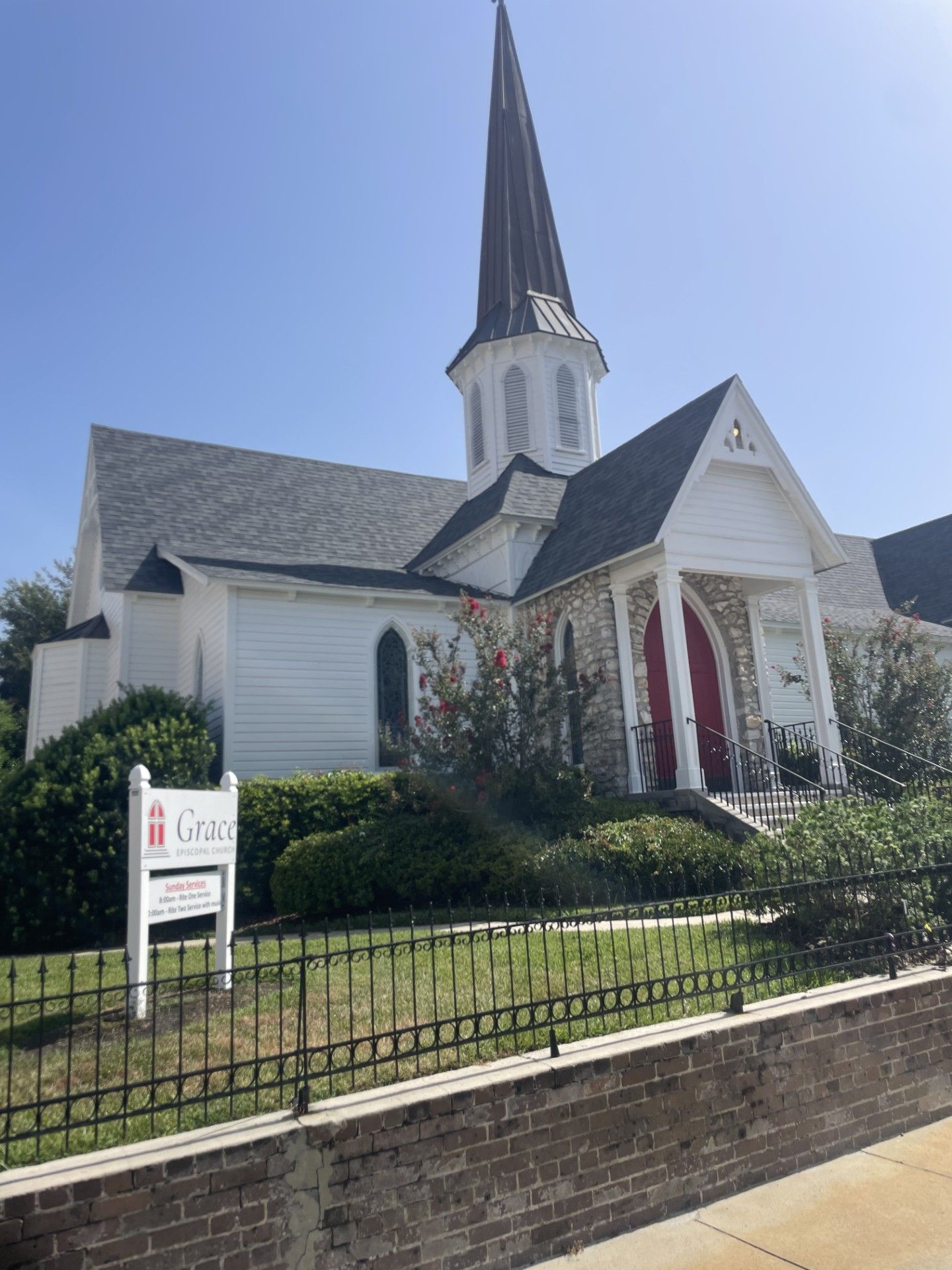 White church with tall steeple and red doors behind a fence on a sunny day