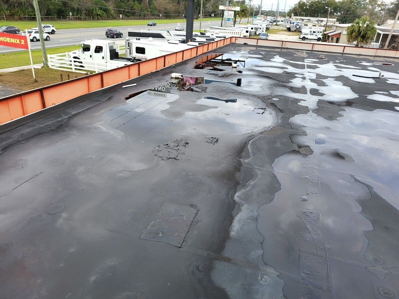 Flat black rooftop with large puddles, orange parapet wall, and parked cars in the background.
