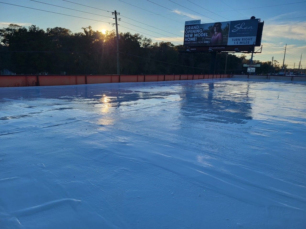 Frozen outdoor rink at sunset with a billboard and power lines in the background