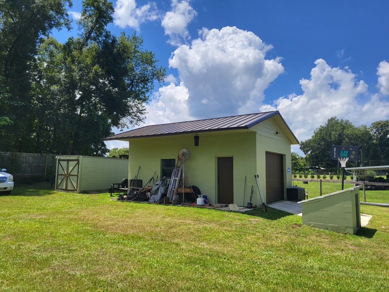Small pale-green house with a tiled roof in a sunny grassy yard under a blue sky with clouds
