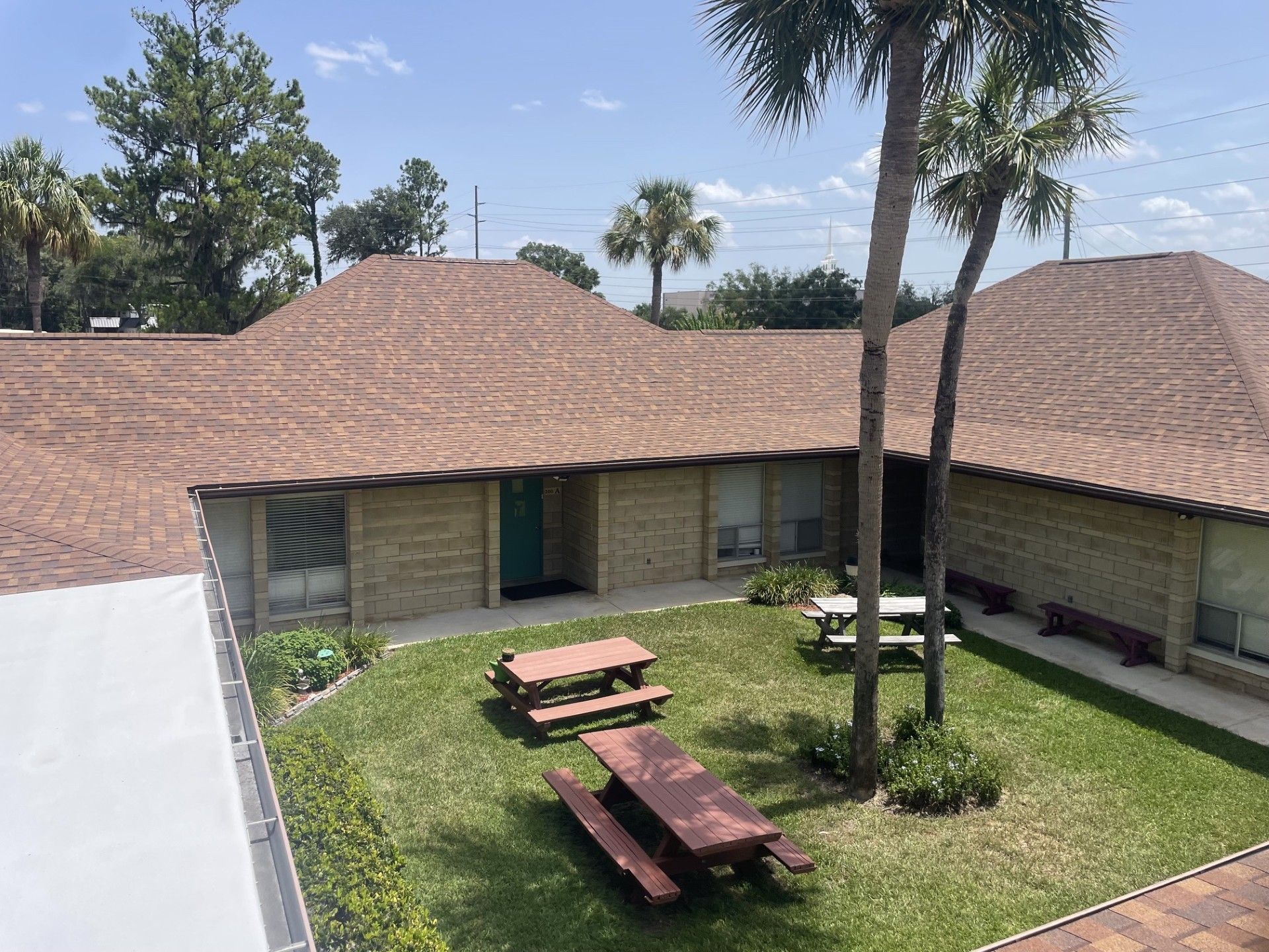 Courtyard with picnic tables, grass, and palm trees beside a tiled-roof building