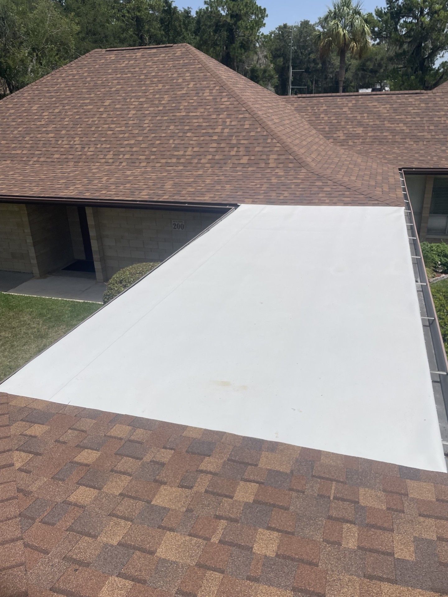 White roof under repair next to a brown shingle roof on a suburban house