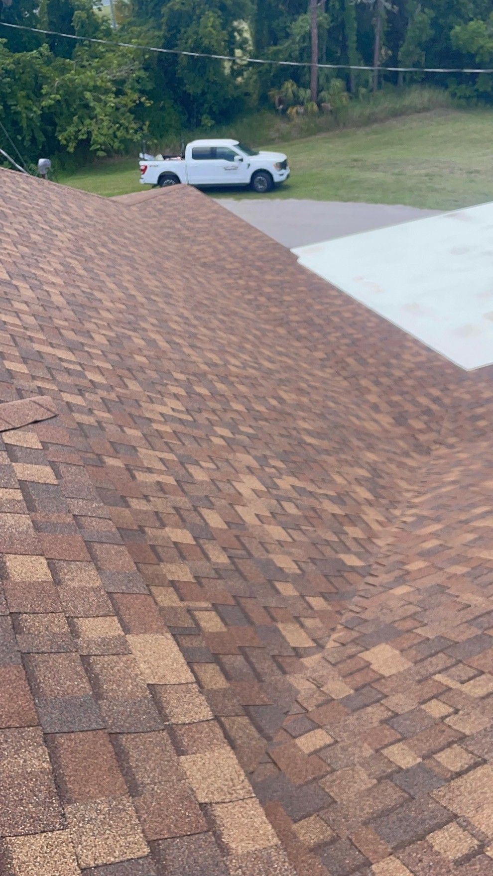 Brown shingled roof in the foreground with a white pickup truck parked on a driveway below.