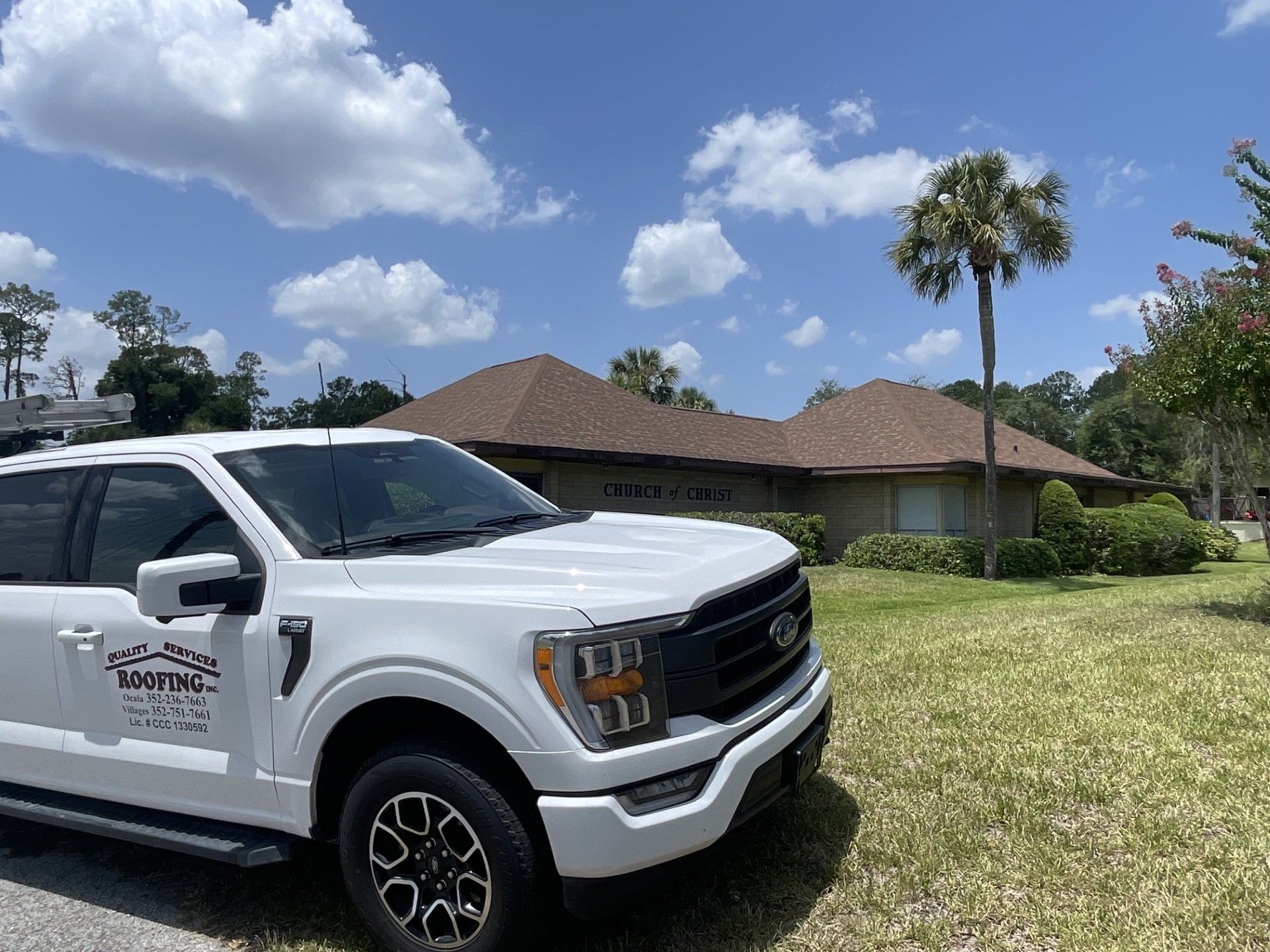White pickup truck with company logo parked on grass in front of a suburban house under a sunny sky
