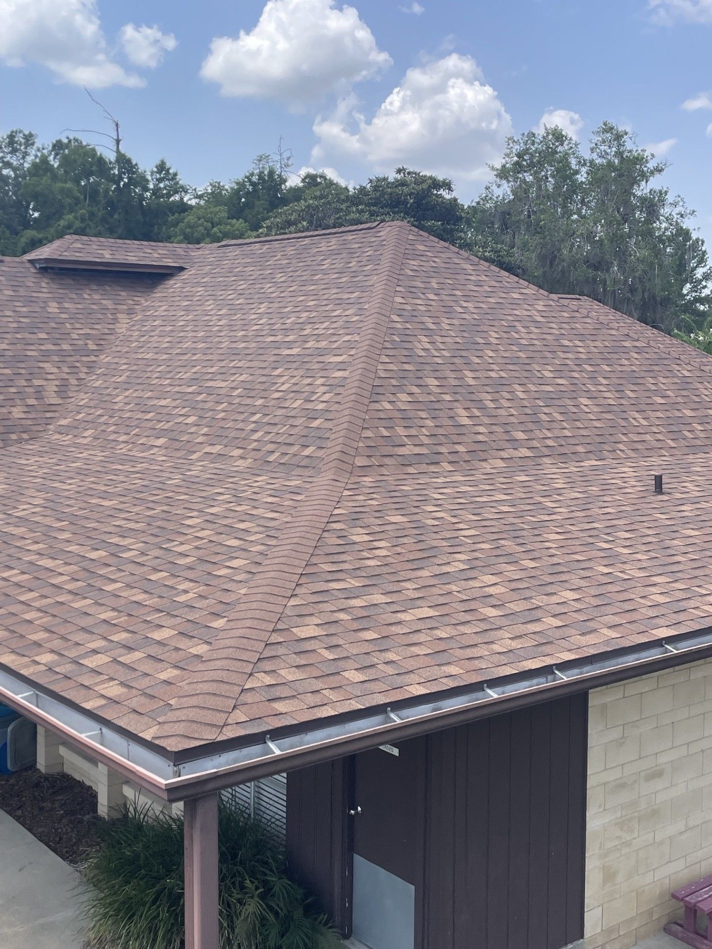 Brown shingled roof on a house with trees and cloudy sky in the background