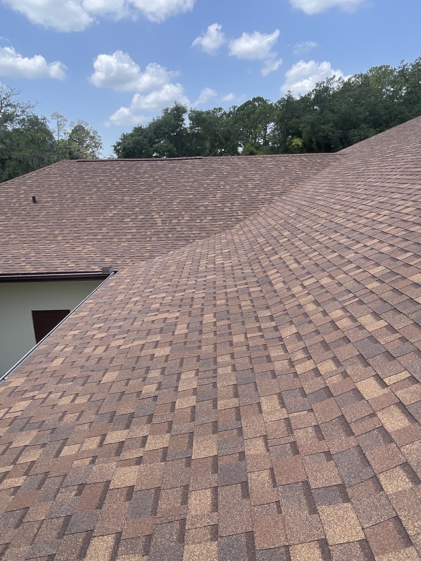 Brown shingle roof with visible slopes under a blue sky with clouds