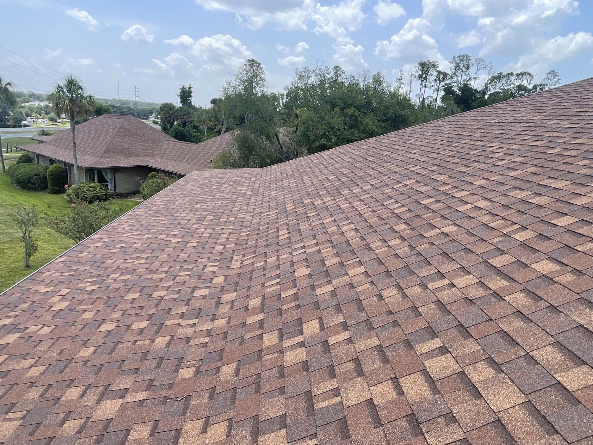 Sloped roof with brown shingles overlooking trees and a distant house under a cloudy sky