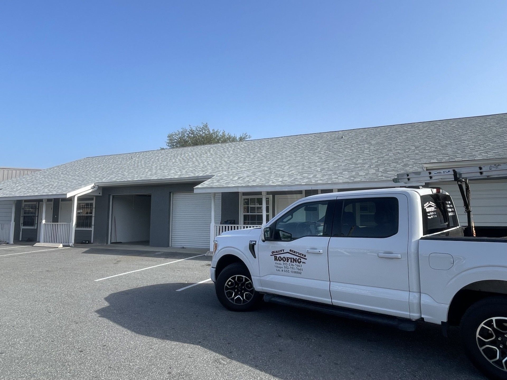 White pickup truck parked outside a light gray building with a shingled roof on a sunny day