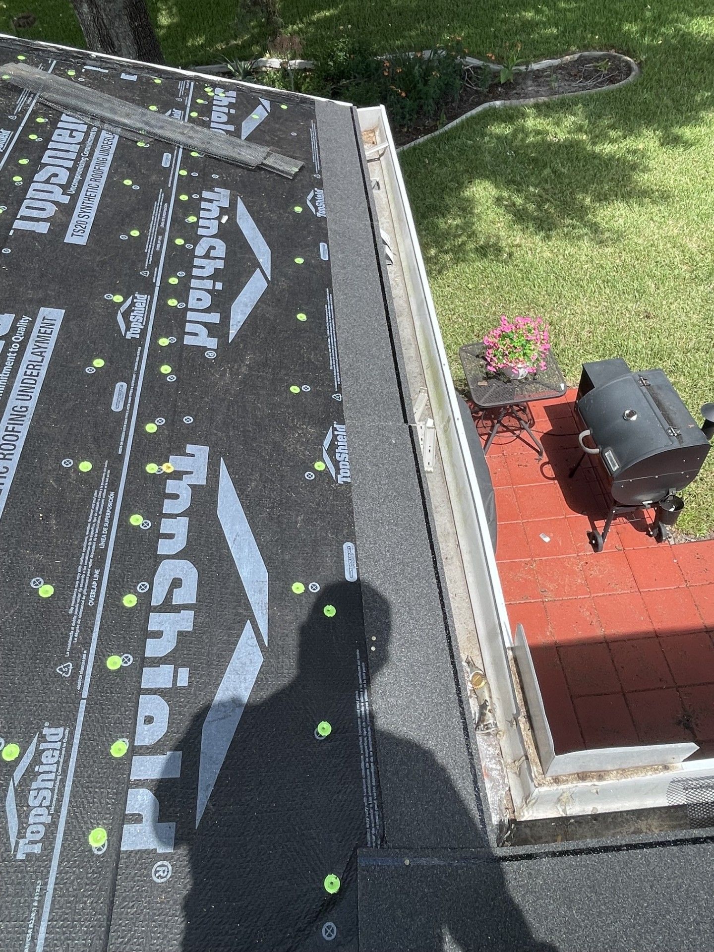 Roofing underlayment on a sloped roof beside a red patio and yard below