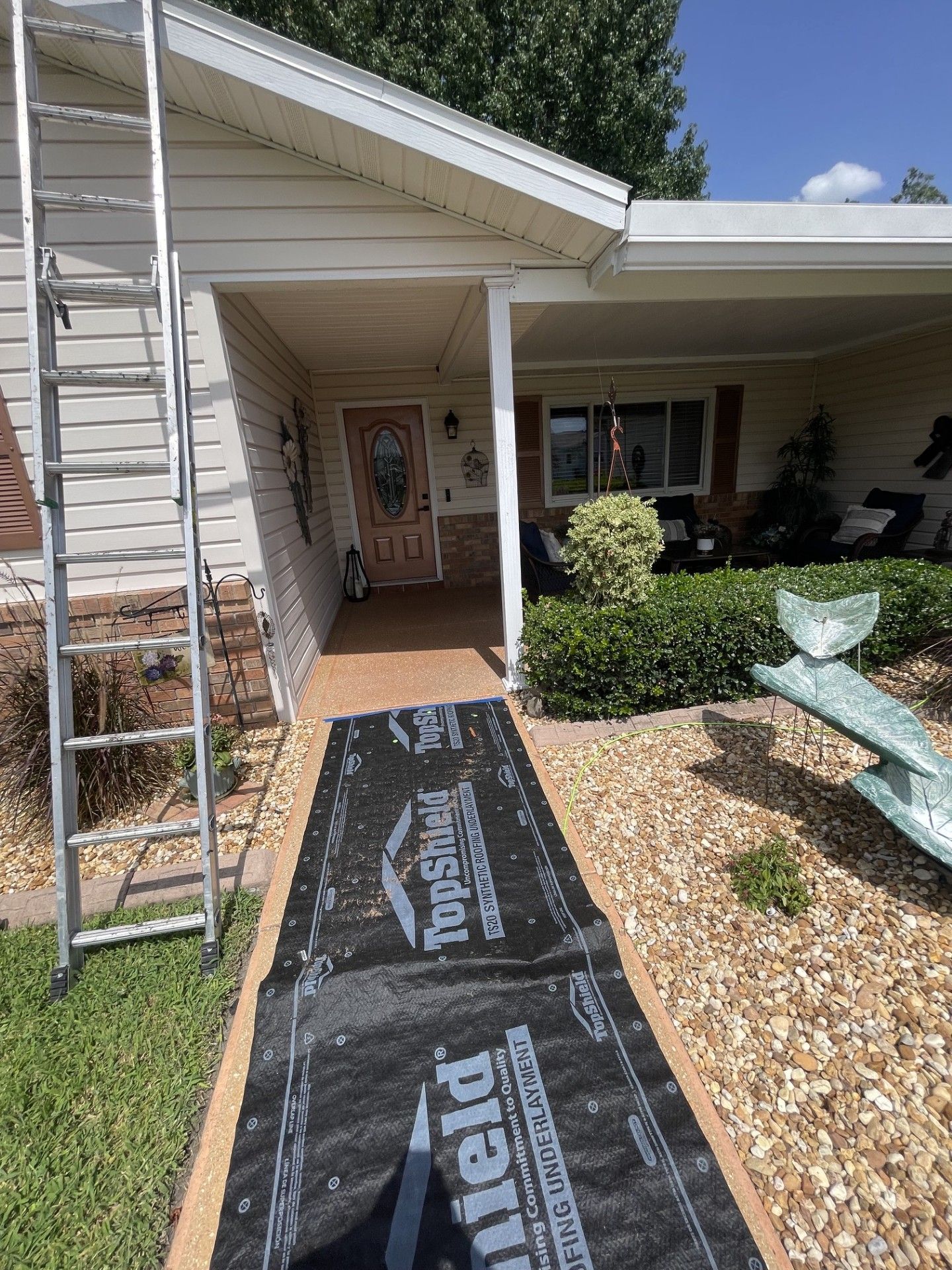 Front porch walkway under construction with black underlayment, ladder on left, and a chair on the right.