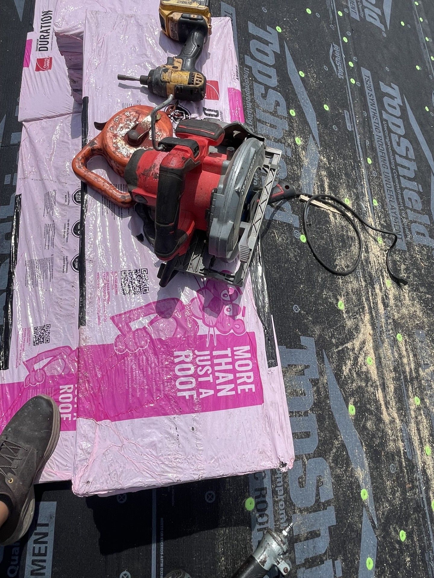 Red chainsaw on pink foam board over a black tarp, with a yellow drill nearby.