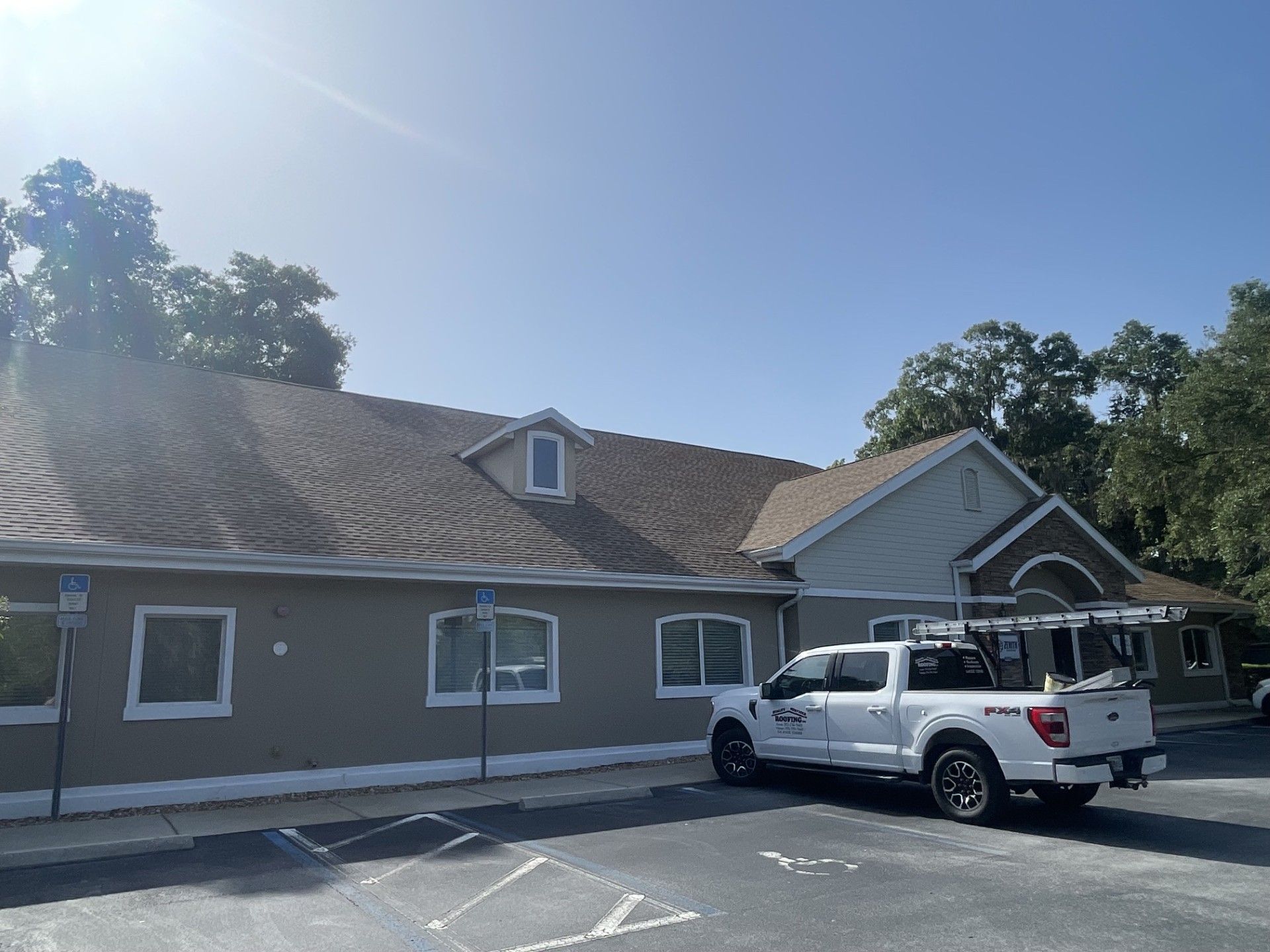 Single-story tan building with white trim and a white pickup truck parked in front under a blue sky