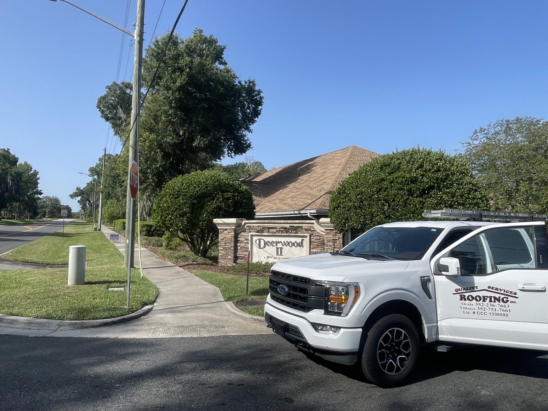 White utility truck parked by a suburban street and a stone entrance sign on a sunny day