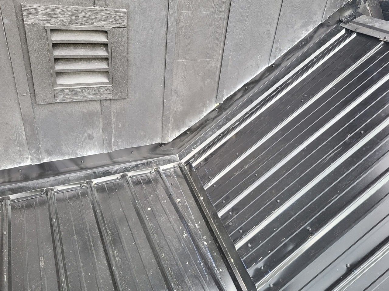 Gray rooftop with metal panels, a wall vent, and a sloped roof corner with white streaks