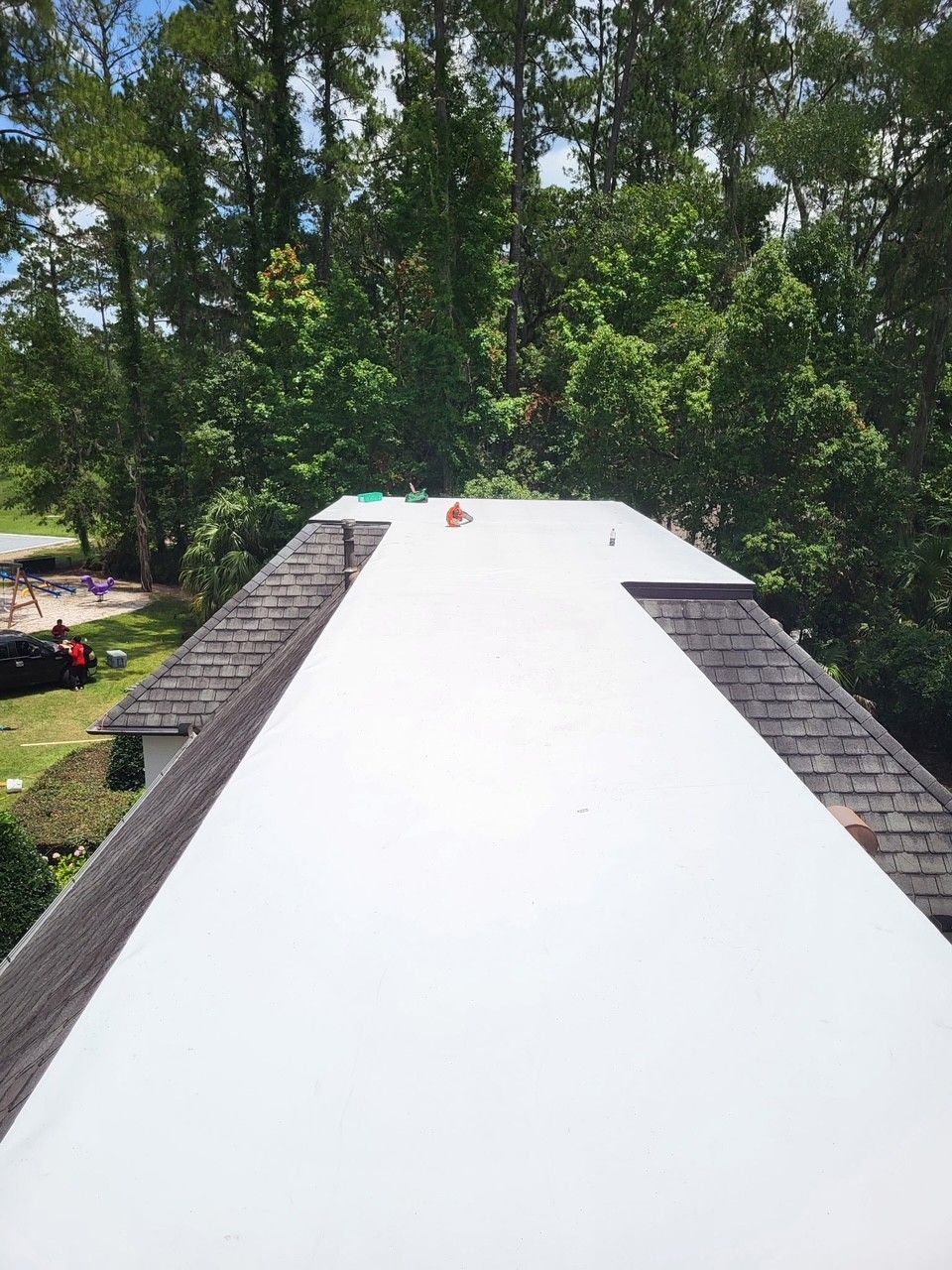 White roof under construction with trees in the background and two small objects near the top edge
