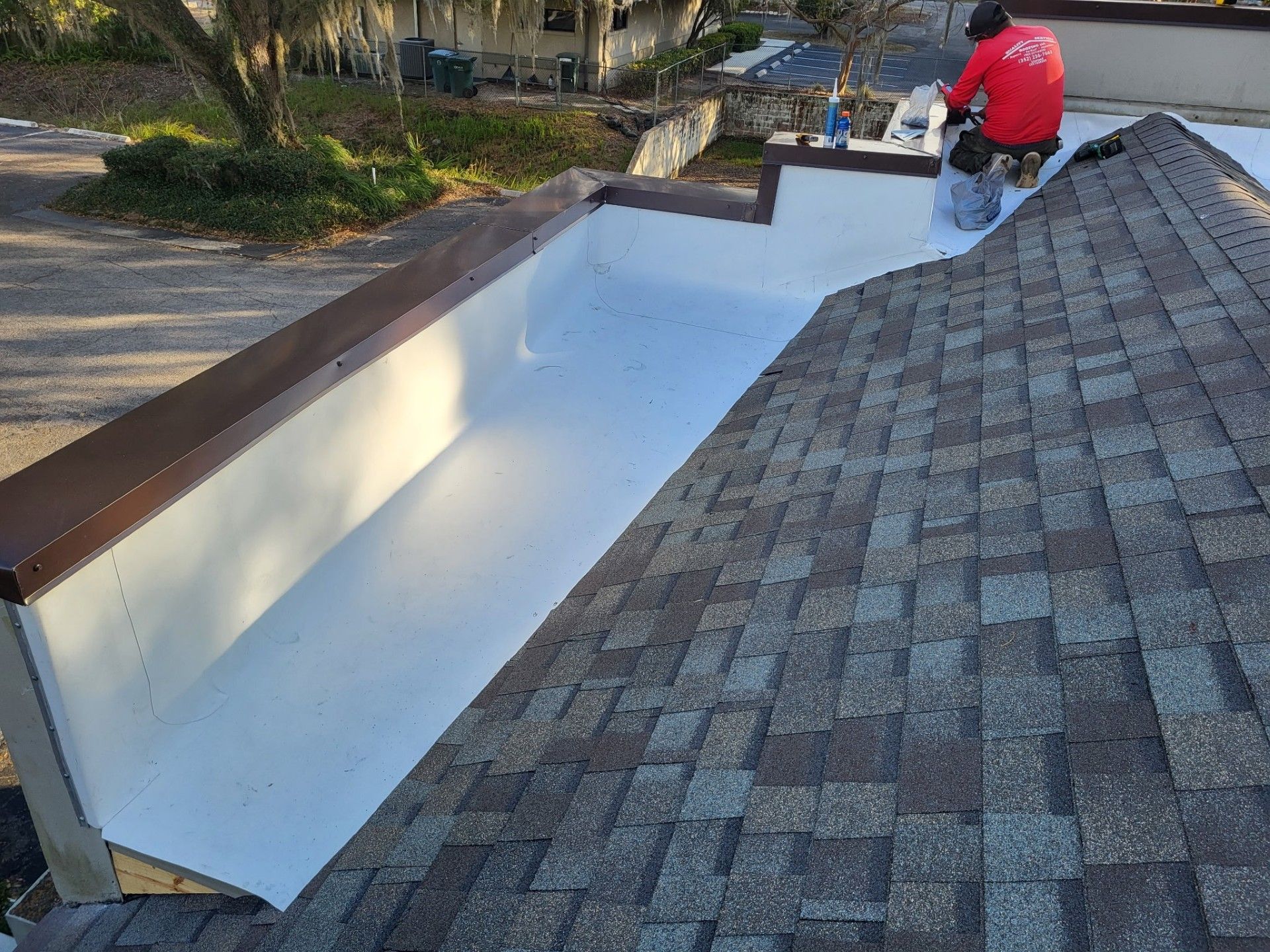 Worker on a shingled roof painting the exterior of a white skylight well white.