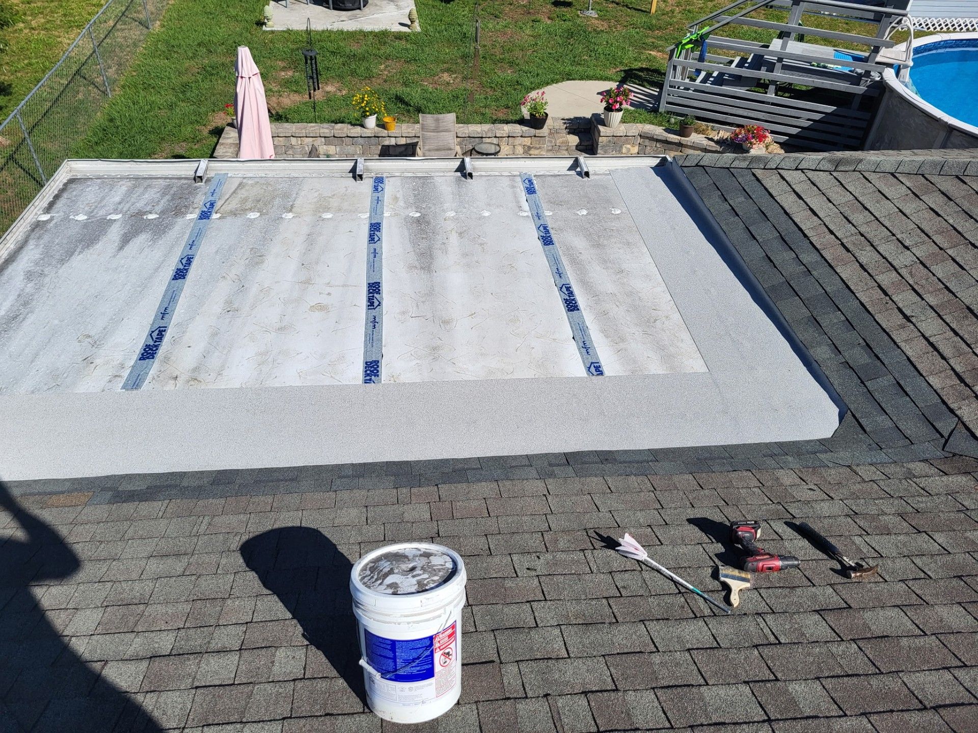 Roof under repair with white waterproof coating, paint can, and tools on asphalt shingles