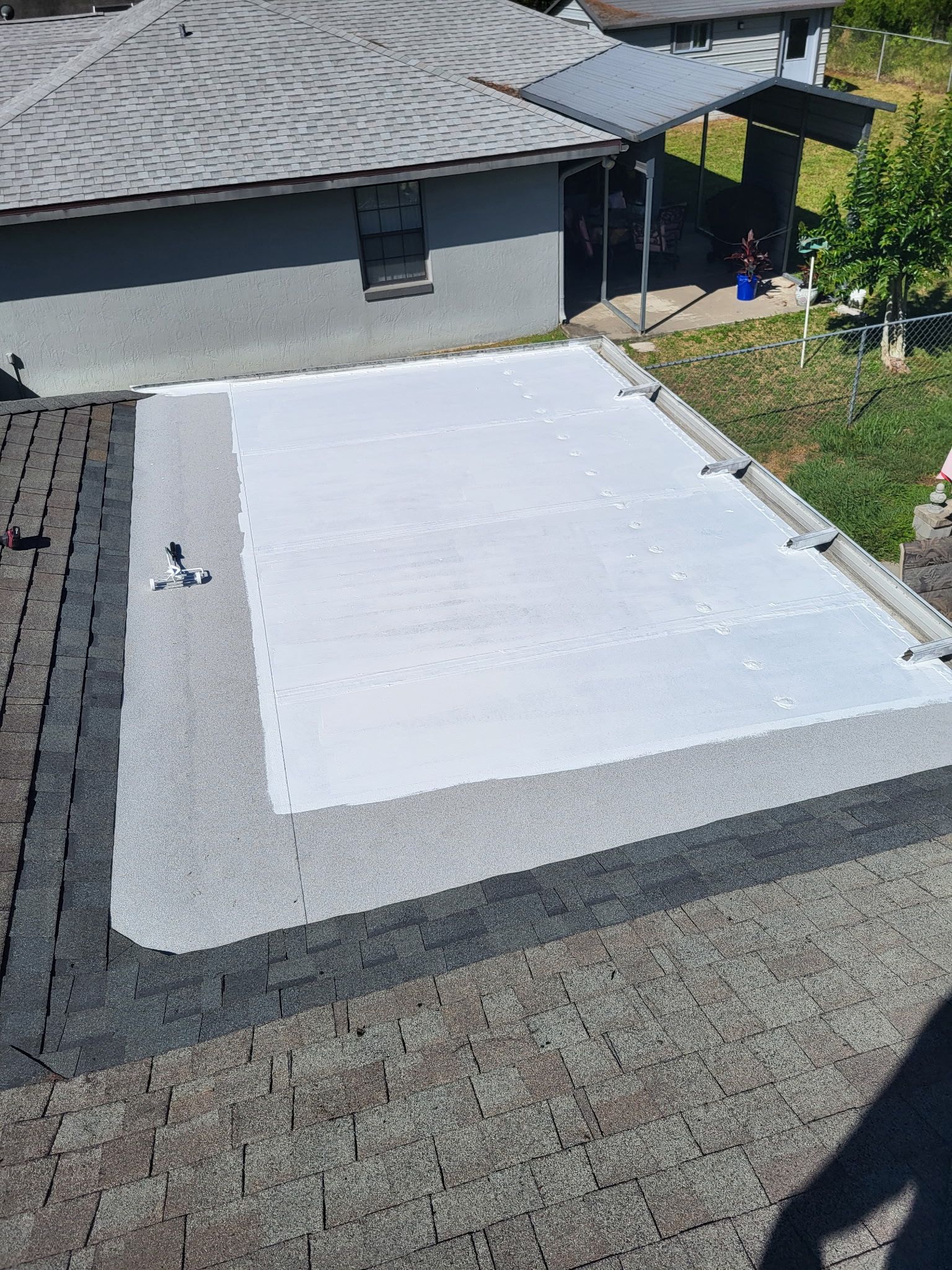 White rooftop solar panel array on a gray shingled roof beside a house and yard
