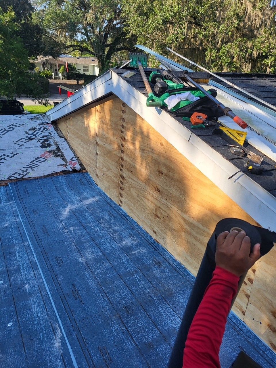 Worker installing roofing on a sloped roof with blue underlayment and exposed wood framing.