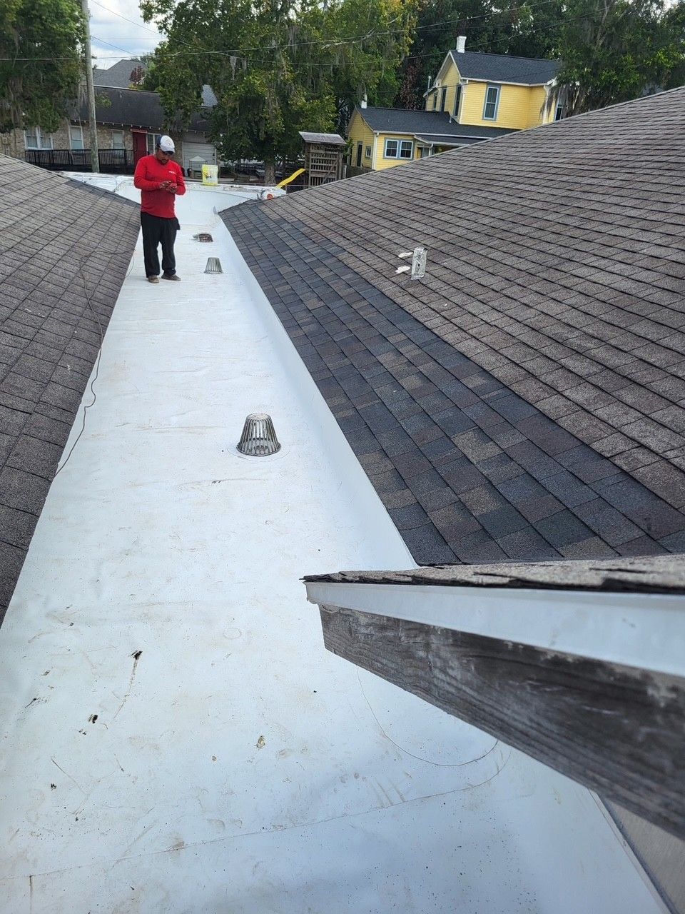 Person in red on a flat roof between shingled sections, looking toward the camera.