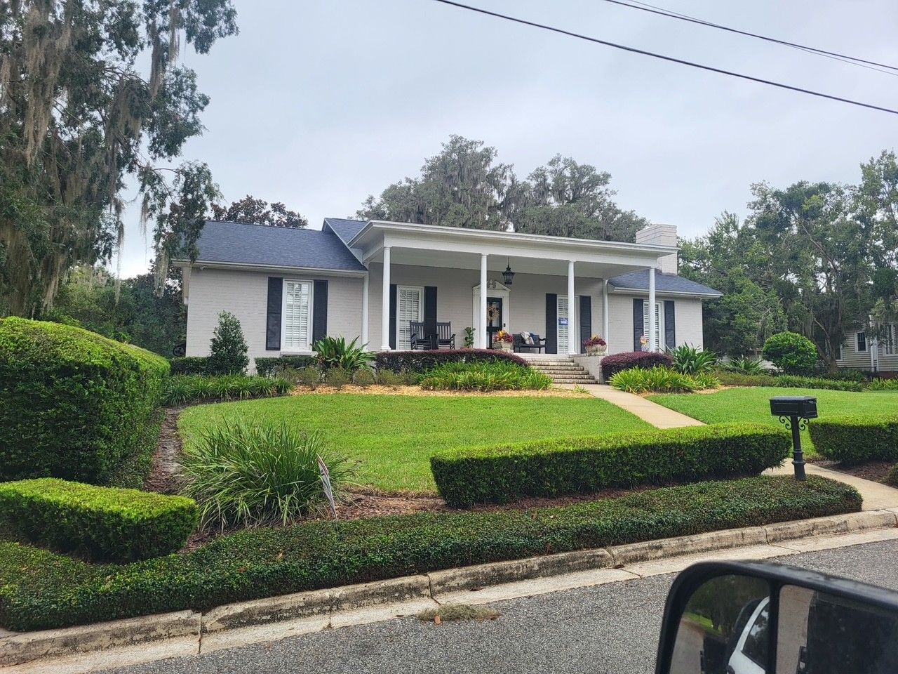 Single-story white house with blue roof, manicured hedges, and a front porch on a quiet street.